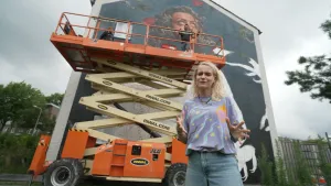 Janouk staat voor hoogwerker met daarachter een muurschildering