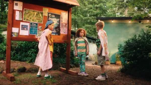 Een foto van 3 kinderen bij een informatiebord op de camping, ze dragen allemaal een soort doek als cape.