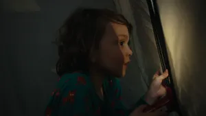 Een foto van een jongetje in een tent, hij gluurt door een rits in de deuropening naar buiten.