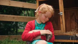 Een meisje zit met een konijntje op school, ze aait het beestje.