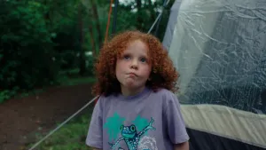 Een foto van een meisje dat voor een tent staat in de regen, ze kijkt bedenkelijk.