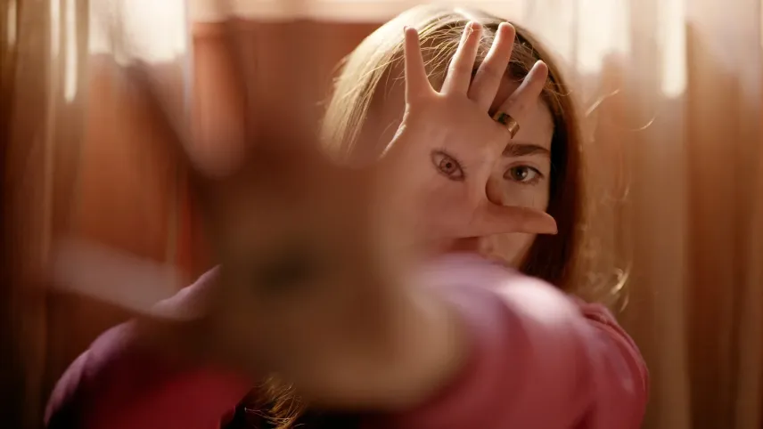 Een close-up foto van een meisje met een hand voor zich uit en een hand voor haar gezicht, op die hand is een oog getekent.