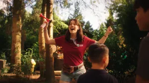 Foto van een vrouw die heel enthousiast kijkt en haar armen omhoog gooit. Ze heeft een toeter in haar ene hand.