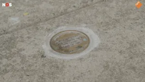 Foto van een ronde bronzen steen met een tekst over een tot slaaf gemaakte in de straat.