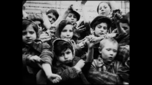 Zwartwitfoto van kinderen die armen uitsteken voor het prikkeldraad van Auschwitz.
