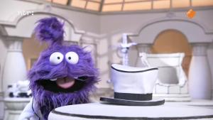 Een foto  van een paar pluizig monster in een zwart-wit kartonnen decor, naast hem op tafel staat een zwart-witte hoed.