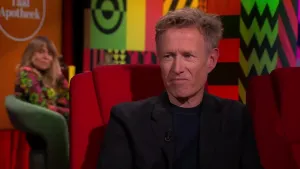 Een foto van schrijver Peter Terrin in een rode stoel in een studio. 