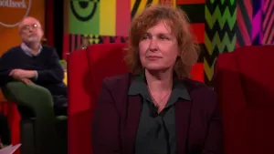 Een foto van schrijfster Annet Schaap in een rode stoel in een studio.