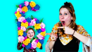 Foto van presentatrice Rosalie naast meisje met verjaardagscijfer zes versierd met kleurrijke bloemen.