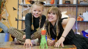 Foto van presentatrice Rosalie met meisje en zelfgeknutselde groene Frankensteinhand met kaars erop.