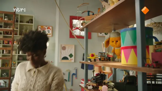 Foto van een jongetje in speelkamer, in rek met speelgoed zit ook Dropje (pop).