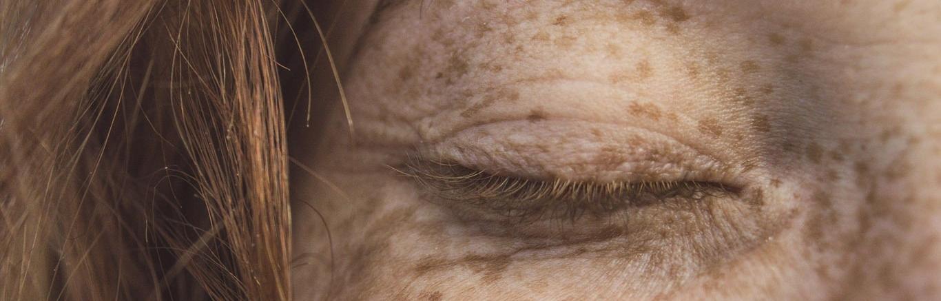 Foto van detail van gezicht van vrouw met rood haar en sproeten, oog is gesloten.