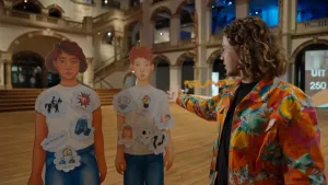 Foto van presentator Pascal naast twee kartonnen afbeeldingen van een meisje en jongen. Er zijn verschillende begrippen op geplakt. Op het meisje: paardrijden, vechten, de baas zijn, jeans, kletsen. Jongen: slim, voetbal, hoge hakken, sieraden, lang haar.