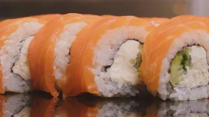 Een foto van sushi. Deze sushi bestaat uit rijstrolletjes met roomkaas in het midden en zalm bovenop.