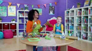 Een foto van de presentatrice en een meisje ze zitten aan tafel te knutselen en moeten erg lachen.