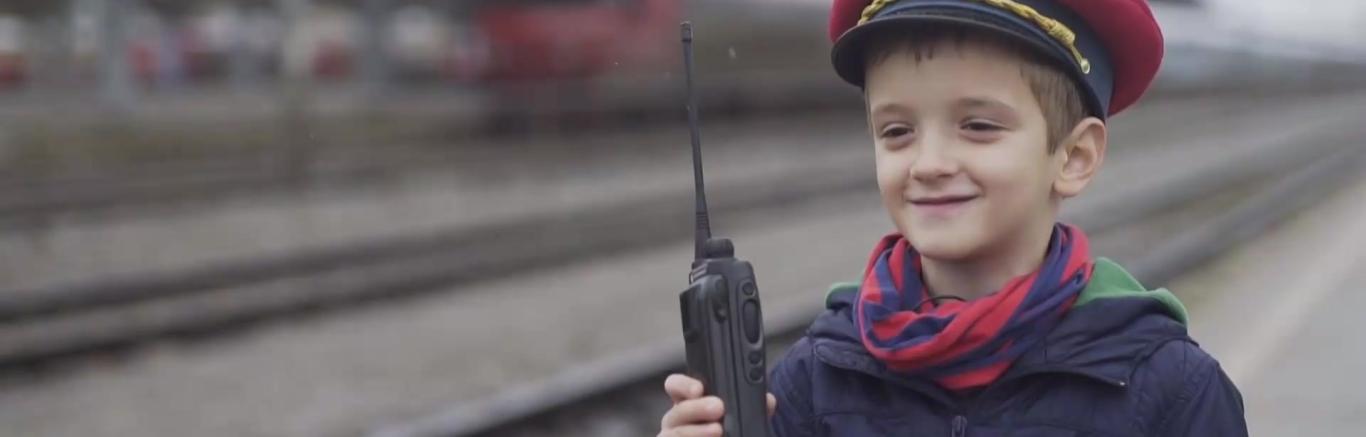 Een foto van een jongetje naast een treinspoor, hij is verkleed als conducteur.