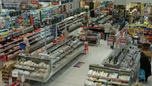 Een foto van een supermarkt van bovenaf gezien, je ziet verschillende koelvakken en een paar mensen die bij de schappen staan.