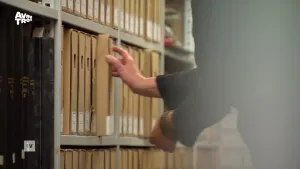 Een foto van een hand die een map uit een archiefkast pakt.