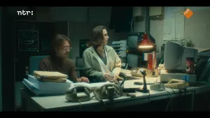 Twee mensen zitten achter een bureau en kijken naar een computer