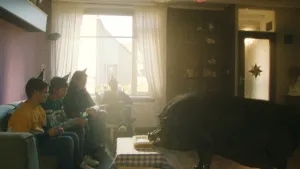 Een aantal kinderen zitten op een bank in een woonkamer. Tegenover hen een varken dat van tafel eet.