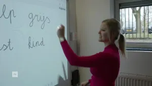 Een foto van een juf die op het digibord schrijft, je ziet de woorden grijs en kind.