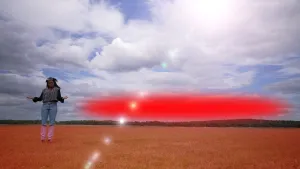 Een foto van presentatrice Eva die in een veld staat. De zon schijnt. Naast haar is een grote rode vlek getekend, die een bel warme lucht voorstelt.