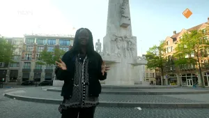 Een foto van presentator Tirsa die voor het monument op de Dam in Amsterdam staat.