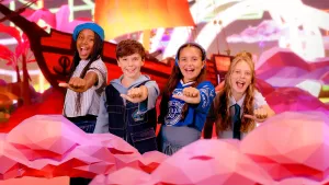 Foto van vier kinderen die blij kijken in een kleurrijke, fantasievolle omgeving. 