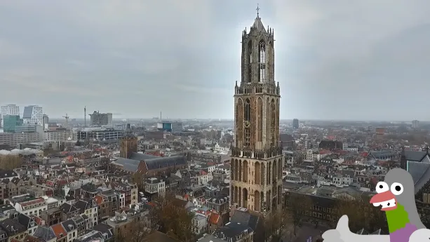Een foto van de Domtoren in Utrecht, een hoge stenen toren met een klok erop. Achter de toren zijn gebouwen in de stad Utrecht te zien, zowel lage oudere huizen als moderne hoge gebouwen. Een getekende duif steekt zijn duim op.