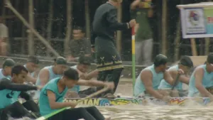 Indonesische roeiers racen op het water. Bovenop een boot staat een man in traditionele kleding.