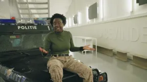 Thirsa zit op een politiewagen. De politiewagen staat binnen in een witte hal.