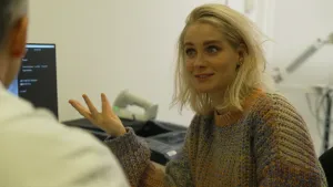 Een foto van presentatrice Janouk in een spreekamer van een arts, je ziet de arts op zijn rug.