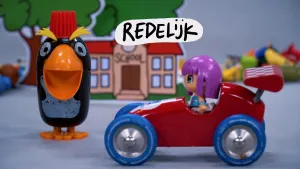 Beeld uit een stopmotionanimatie met speelgoedpoppetjes op blauwe achtergrond. Een poppetje met paars haar zit in een rode sportauto met ernaast een pinguinpoppetje voor een schoolgebouw. In de lucht staat het woord 'redelijk'.