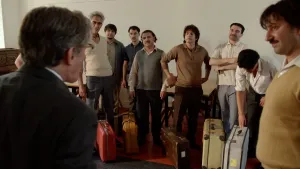 Foto van Turkse mannen met koffers die worden toegesproken door Amsterdamse wethouder in jaren 70.