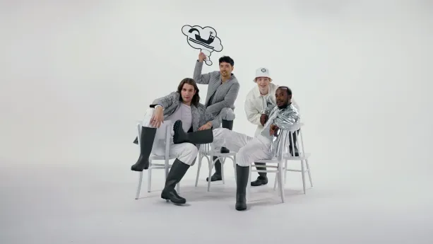 Foto van vier wit en zilver geklede jongens op witte achtergrond die in stoere houdigen poseren op stoelen.