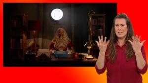 Sinterklaas zit achter zijn bureau. De gebarentolk staat naast het scherm.