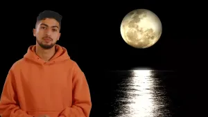 De presentator (man) is te zien met op de achtergrond een maan waarvan het licht op de zee weerspiegelt.