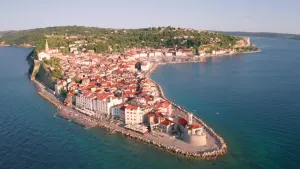 Een foto van een sloveens schiereiland, op de punt die in het water steekt, staan huizen verder naar achteren zie je meer groen.