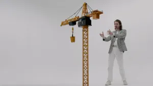 Foto van jongen in witte en zilveren outfit naast een gele speelgoedhijskraan.