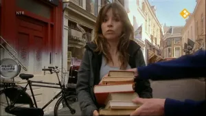 Foto van presentator in een straat met boeken in haar hand.