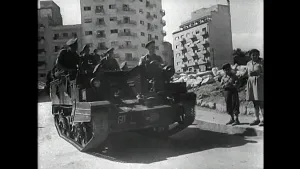 Een tank met daarop soldaten rijdt door een straat.