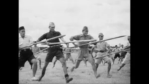 Zwart-wit beeld van een aantal rennende Indonesische mannen met speren in hun handen.