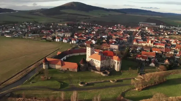 Een foto van een Tsjechisch landschap met heuvels en vooraan een stadje met een burcht.