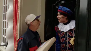 Hoofdpiet staat in de deuropening, voor de deur staat de postbode met een pakketje.