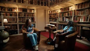 Twee mensen zitten in bruine stoelen in een bibliotheek.