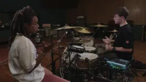 De drummer legt uit aan de presentator hoe de elektronische drumpads werken.