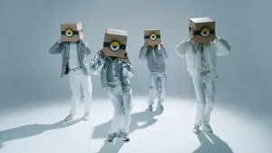 Foto van vier in het wit en zilver geklede jongens met een kartonnen doos op hun hoofd waarop een oog van een minion staat.