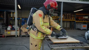 Foto van brandweerman in kaki pak en rode helm die met handschoenen aan een tablet op een kookplaat legt.