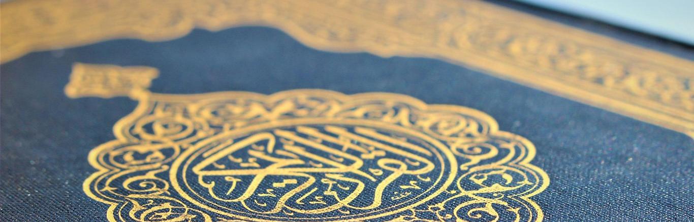 Foto van de omslag van een Koran, donkerblauw met gouden tekens.
