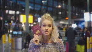 Een foto van presentatrice Janouk met een paspoort in haar hand, ze houd het paspoort naast haar gezicht.